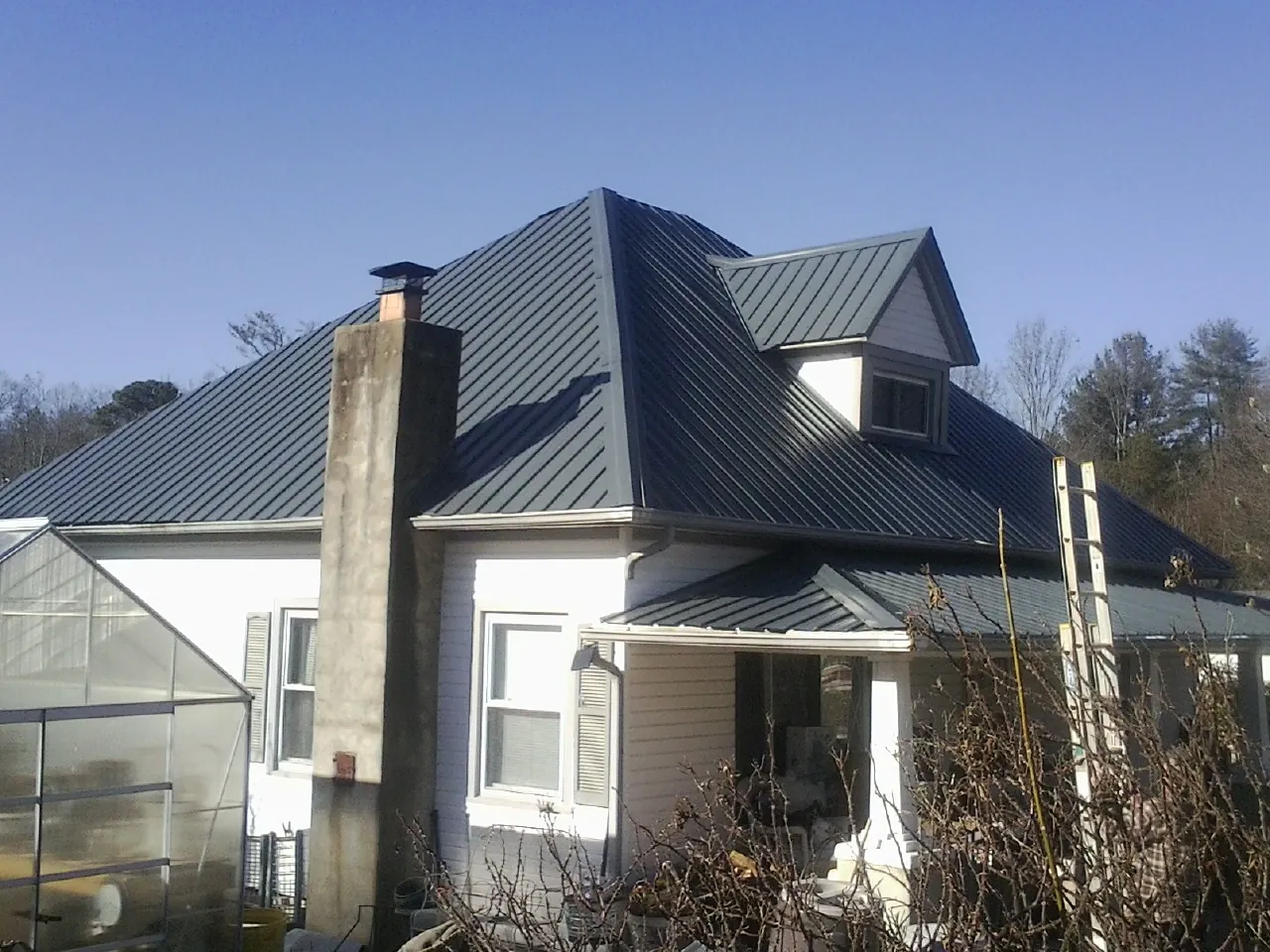 Dark blue standing seam metal roof on a white farmhouse with dormer — Slate & Tile Roof Repair by Roofing Brothers in Greentown
