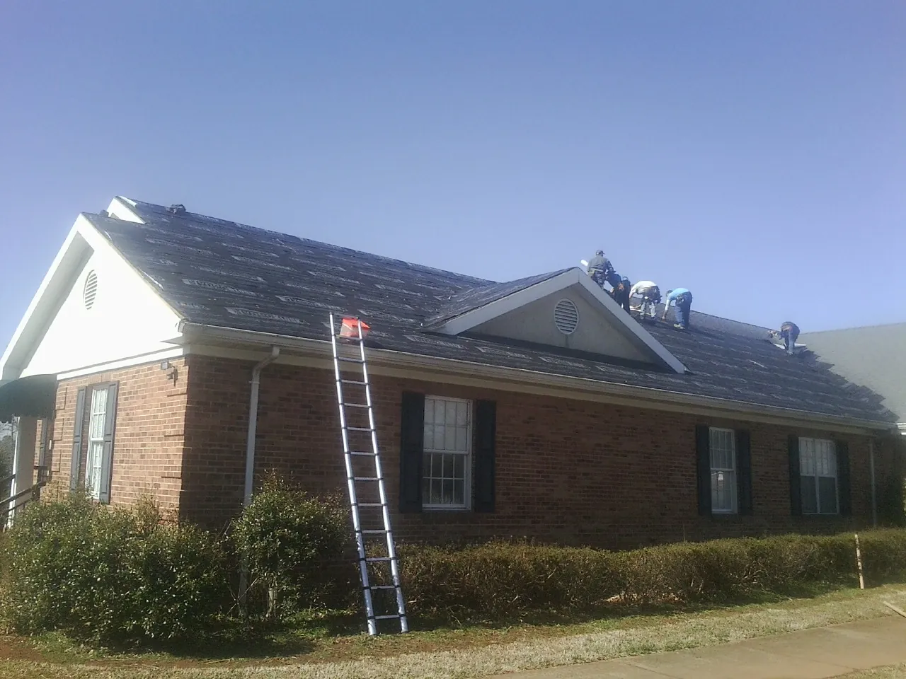 Crew tearing shingles off a brick ranch roof with a ladder set — Emergency Roof Repair work by our crew in Greentown
