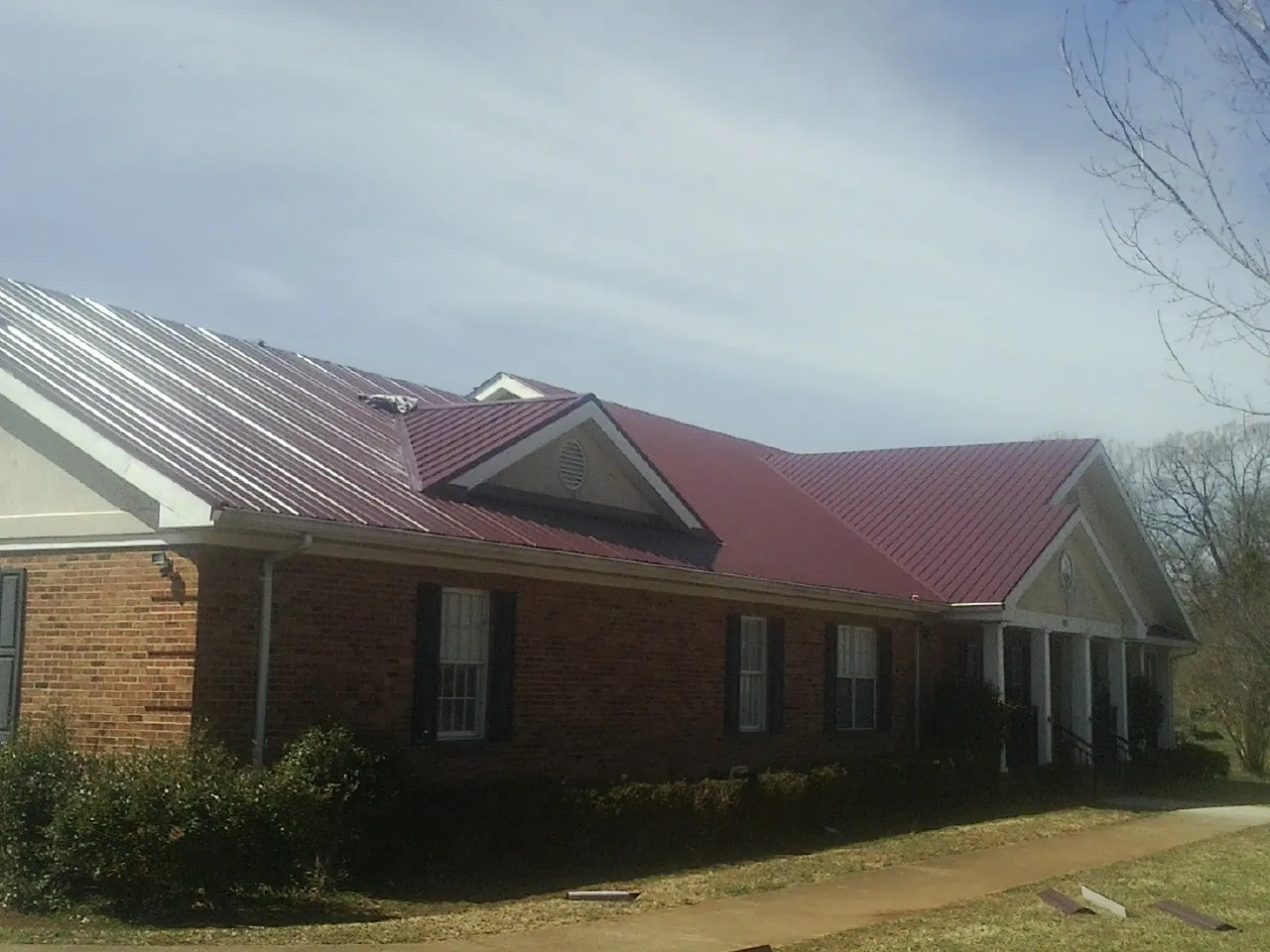 Red metal roof with gabled entries on a long brick building, from a Hail Damage Roof Repair job in Greentown