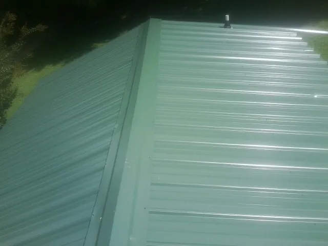New green metal panels meeting at the ridge of a roof — Flat Roof Repair work by our crew in Greentown