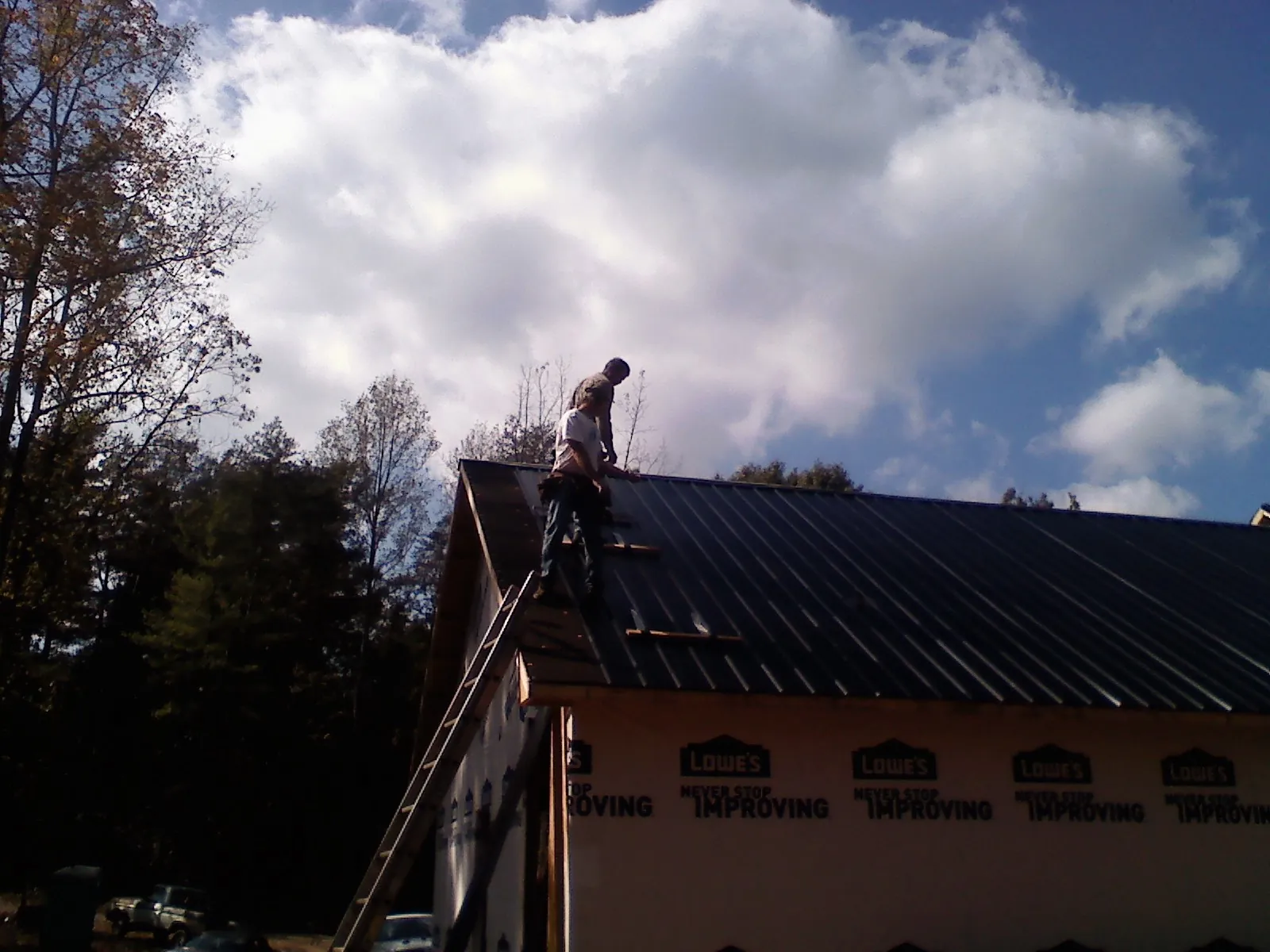 Roofer fastening dark metal panels high against a cloudy sky, from a Roof Inspection job in Greentown