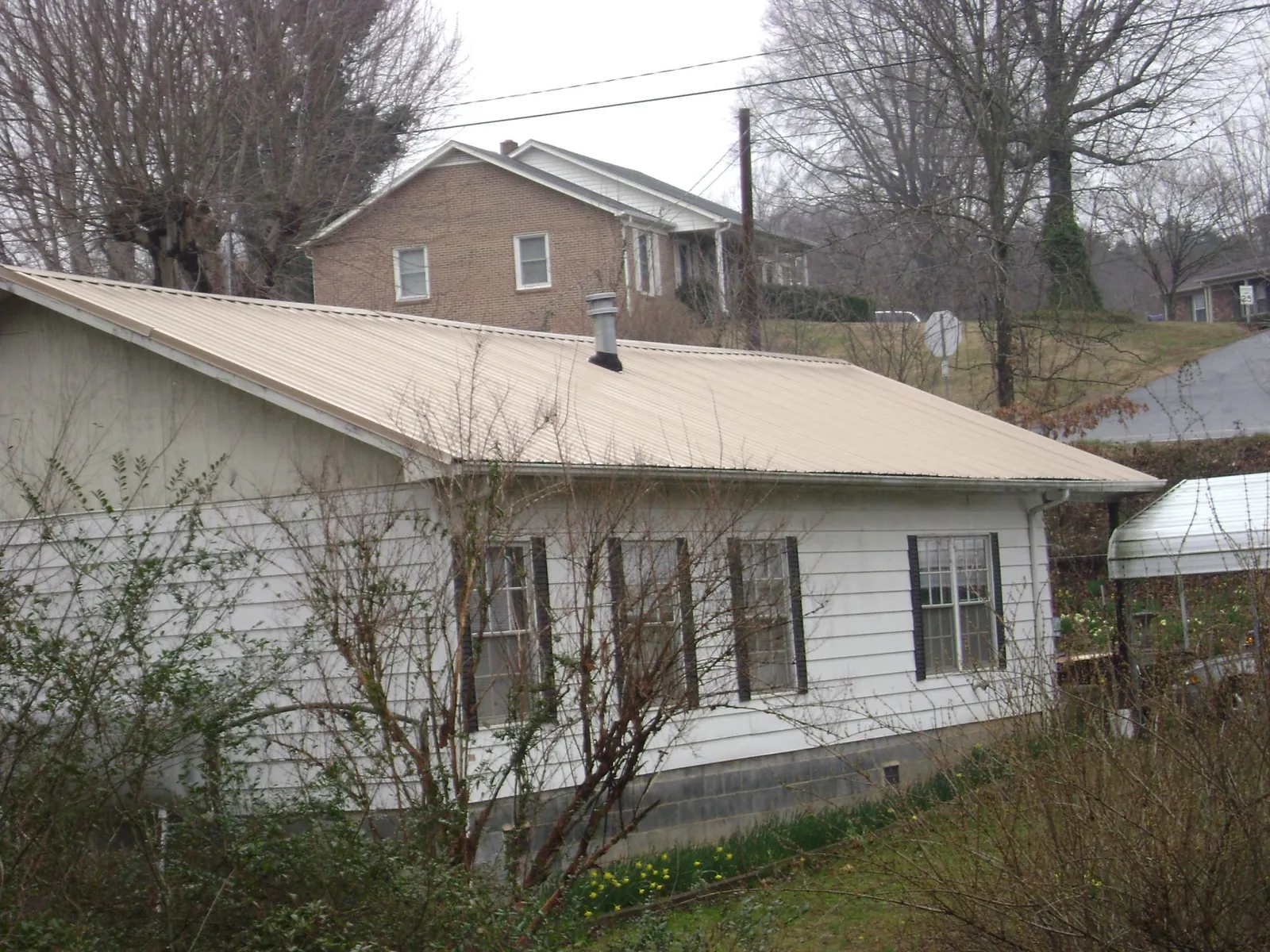 Tan metal roof on a white sided house set into a hillside — Commercial Roofing by Roofing Brothers in Greentown