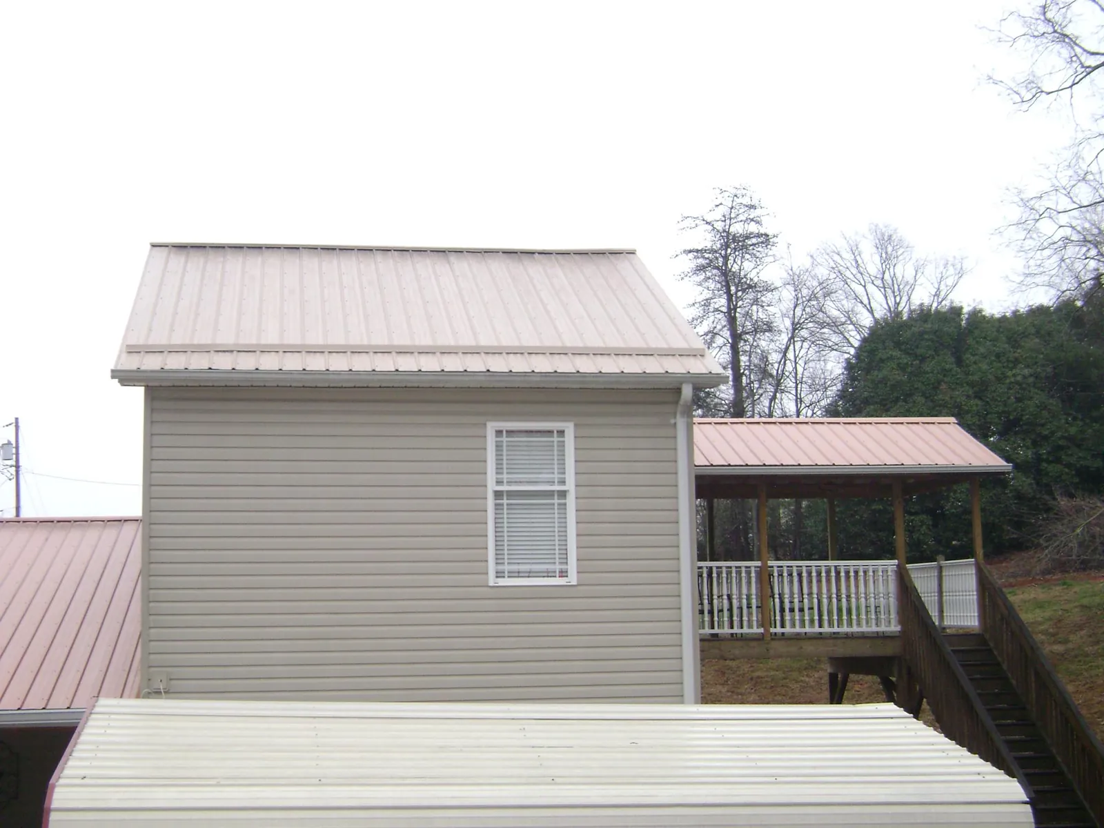 Tan metal roofs on a two story addition and attached porch, from a Roof Replacement job in Greentown